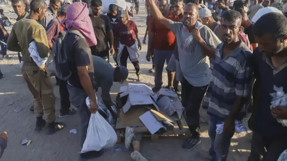 Palestinians stand next the body of a woman who was hit by a truck while attempting to reach a humanitarian aid convoy moving along the Morag corridor near Rafah, in the southern Gaza Strip, Monday, Aug. 4, 2025. (AP Photo/Mariam Dagga)